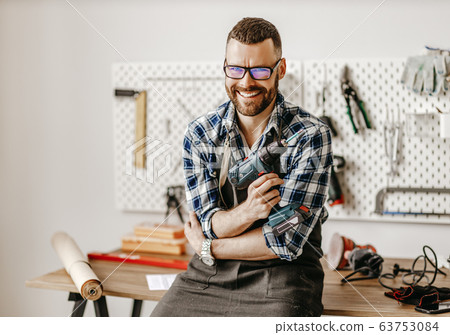 Cheerful craftsman with drill looking at camera Cheerful craftsman with drill looking at camera 63753084