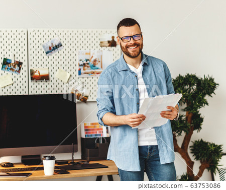 Cheerful man with papers standing at workplace Cheerful man with papers standing at workplace 63753086