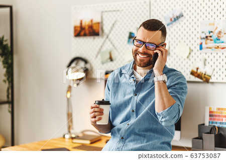 Cheerful man with cup of coffee talking on phone 63753087