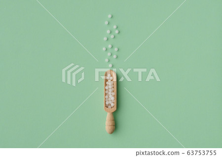 Wooden scoop of homeopathic granules on green 63753755