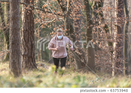 Corona virus, or Covid-19, is spreading all over the world. Portrait of caucasian sporty woman wearing a medical protection face mask while running in nature. Corona virus, or Covid-19, is spreading all over the world. Portrait of caucasian sporty woman wearing a medical protection face mask while running in nature. 63753948