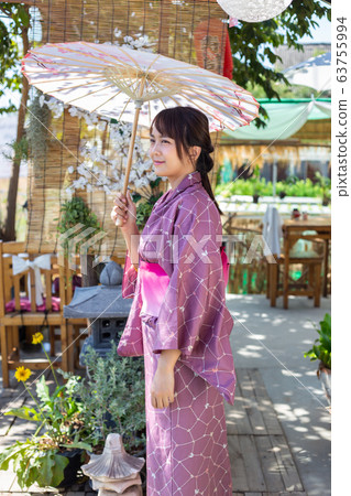 The girl is wearing a pink traditional yukata, which is the national dress of Japan and Hold an umbrella The girl is wearing a pink traditional yukata, which is the national dress of Japan and Hold an umbrella 63755994