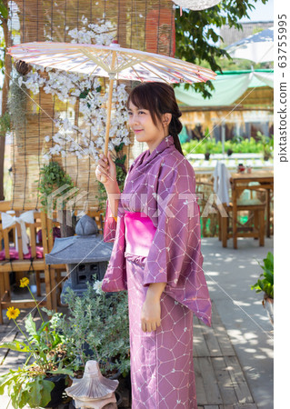 The girl is wearing a pink traditional yukata, which is the national dress of Japan and Hold an umbrella The girl is wearing a pink traditional yukata, which is the national dress of Japan and Hold an umbrella 63755995