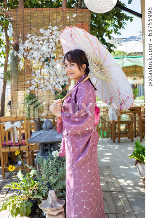 The girl is wearing a pink traditional yukata, which is the national dress of Japan and Hold an umbrella The girl is wearing a pink traditional yukata, which is the national dress of Japan and Hold an umbrella 63755996