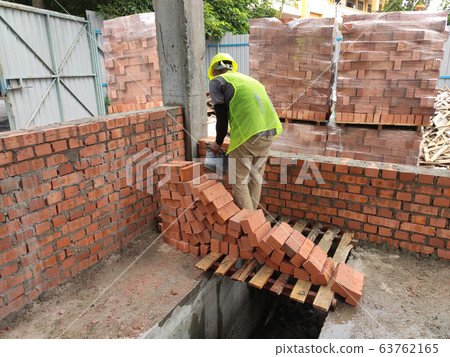 Brickwork by construction workers at the construction site. Workers laying the clay brick and stacked it together using mortar to form the wall.  63762165