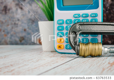 calculator and stacking coin squeezing in a G-clamp on wooden desk calculator and stacking coin squeezing in a G-clamp on wooden desk 63763533
