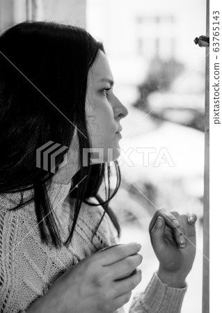 Black and white profile portrait of a brunette woman looking through a window. Selective focus Black and white profile portrait of a brunette woman looking through a window. Selective focus 63765143