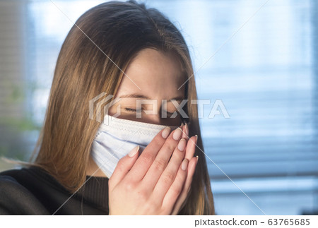 Prevent the spread of the Coronavirus Disease. Young woman sneezing or coughing in a protective medical face mask Prevent the spread of the Coronavirus Disease. Young woman sneezing or coughing in a protective medical face mask 63765685