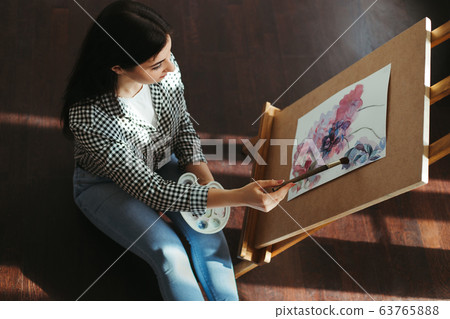 Woman painting with watercolor holding palette Woman painting with watercolor holding palette 63765888