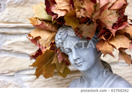 Stone head of a young female sculpture with autumn leaves wreath. Stone head of a young female sculpture with autumn leaves wreath. 63768262