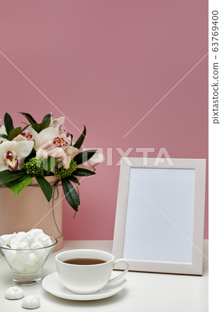 Front view blank mock up of photo frame on the pink background. orchid flowers, cup of tea and sweets. Space for text Front view blank mock up of photo frame on the pink background. orchid flowers, cup of tea and sweets. Space for text 63769400