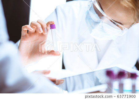 Coronavirus pandemic. Professional female scientist in protective eyeglasses researching tube in laboratory. Concepts of medicine and virus protection Coronavirus pandemic. Professional female scientist in protective eyeglasses researching tube in laboratory. Concepts of medicine and virus protection 63771900