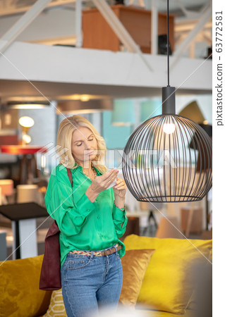 Blonde woman in a green blouse standing near the cage with a bird 63772581