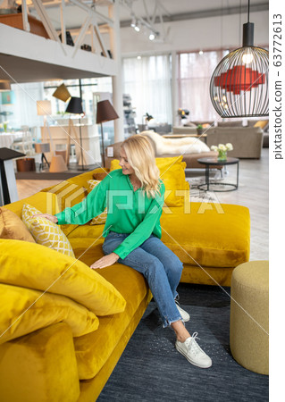 Blonde woman in a green blouseand jeans sitting on a sofa Blonde woman in a green blouseand jeans sitting on a sofa 63772613