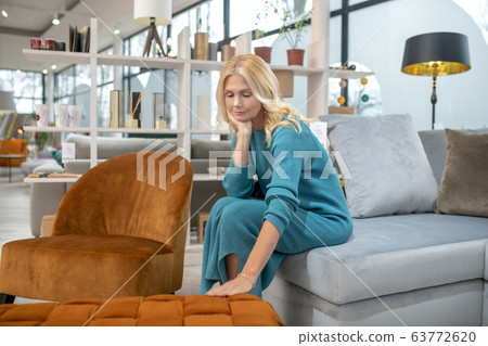 Blonde woman in a blue dress touching the sofa 63772620