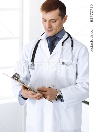 Doctor man using clipboard for filling up medication history record. Perfect medical service. Physician at work in clinic. Medicine and healthcare concepts Doctor man using clipboard for filling up medication history record. Perfect medical service. Physician at work in clinic. Medicine and healthcare concepts 63772750