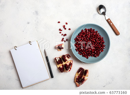 Grains of peeled pomegranate lie in a plate. Top view. Close-up. A book for writing recipes lies on the table. Copy space for text. 63773160