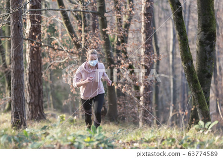 Corona virus, or Covid-19, is spreading all over the world. Portrait of caucasian sporty woman wearing a medical protection face mask while running in nature. Corona virus, or Covid-19, is spreading all over the world. Portrait of caucasian sporty woman wearing a medical protection face mask while running in nature. 63774589