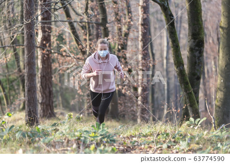 Corona virus, or Covid-19, is spreading all over the world. Portrait of caucasian sporty woman wearing a medical protection face mask while running in nature. Corona virus, or Covid-19, is spreading all over the world. Portrait of caucasian sporty woman wearing a medical protection face mask while running in nature. 63774590