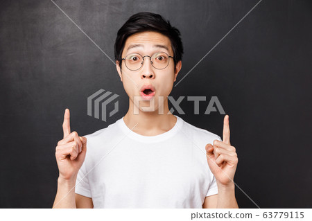 Close-up portrait of amused and excited happy asian man visit amusement park for first time, pointing fingers up at something super cool, say wow astonished, stand black background Close-up portrait of amused and excited happy asian man visit amusement park for first time, pointing fingers up at something super cool, say wow astonished, stand black background 63779115