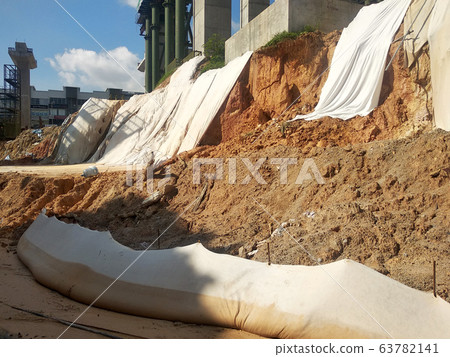 The geotextile fabric is spread over the surface of the slope to prevent erosion. Also to temporarily stabilize the slope before the permanent stabilization work done. 63782141