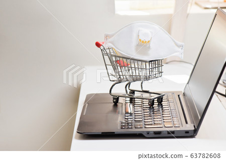 Conceptual photo with miniature shopping-cart and protecting mask. Safety internet shopping Conceptual photo with miniature shopping-cart and protecting mask. Safety internet shopping 63782608