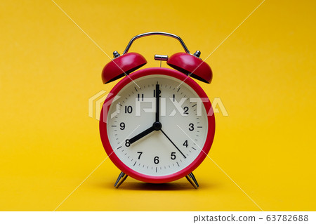 Close up red alarm clock on yellow background Close up red alarm clock on yellow background 63782688