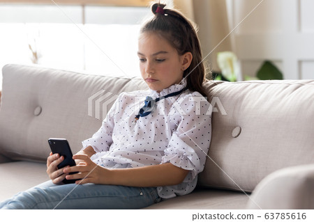 Serious little schoolgirl using smartphone mobile apps alone at home. Serious little schoolgirl using smartphone mobile apps alone at home. 63785616