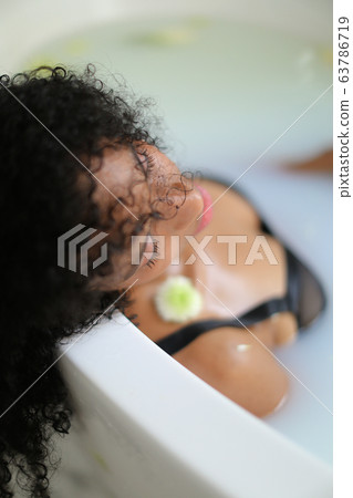 Portrait of curly haired black girl lying in milk bath and wearing bra. 63786719