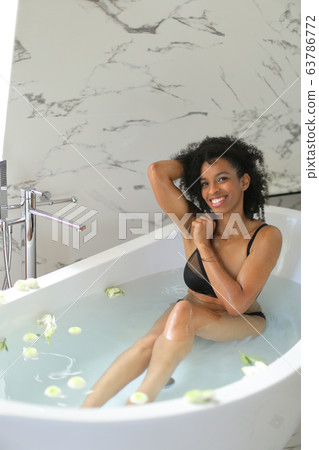 Black happy girl lying in bath with flowers and wearing underwear. 63786772