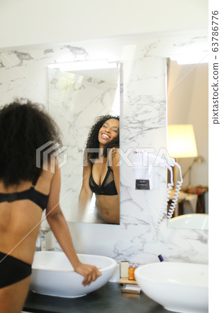 Back view black smiling girl looking at mirror reflection in bathroom. Back view black smiling girl looking at mirror reflection in bathroom. 63786776