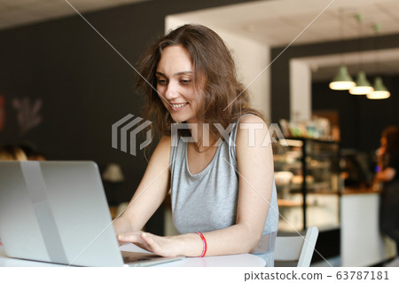 Young smiling woman making video call by laptop at cafe. Young smiling woman making video call by laptop at cafe. 63787181