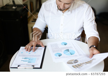 Caucasian confident businessman working with documents and diagrams. Caucasian confident businessman working with documents and diagrams. 63787203
