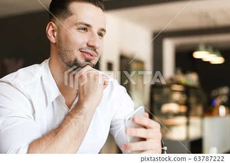 Young handsome businessman using smartphone at cafe. Young handsome businessman using smartphone at cafe. 63787222