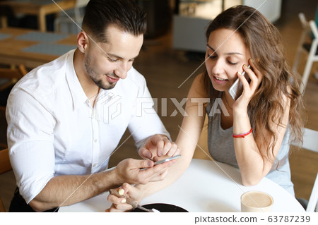Young woman talking by smartphone and sitting with man using hotspot at cafe. Young woman talking by smartphone and sitting with man using hotspot at cafe. 63787239