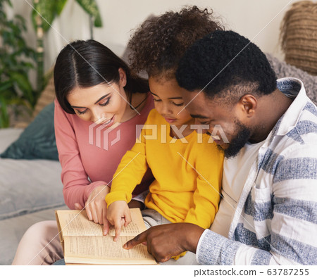 Parents helping daughter read book at home 63787255