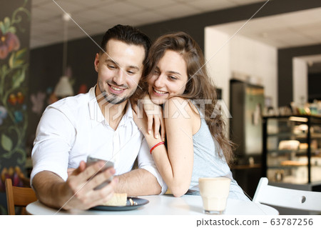 Young woman sitting with man using smartphone at cafe and eating cake. 63787256