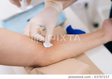 Nurse treats the patient's arm with alcohol cotton wool before taking blood. 63787257