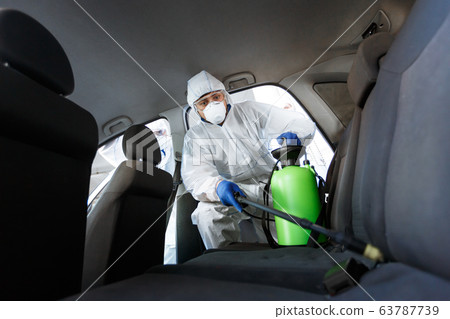 Man in protective suit disinfecting with chemicals his car 63787739