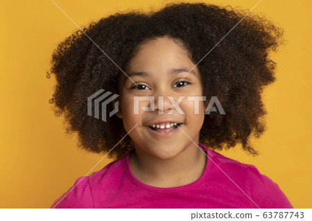 Curly Little Black Girl Smiling At Camera, Posing On Yellow Background 63787743