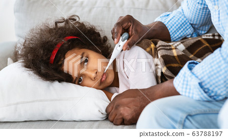 Infectious disease concept. Ill African American child and her grandfather with thermometer at home Infectious disease concept. Ill African American child and her grandfather with thermometer at home 63788197