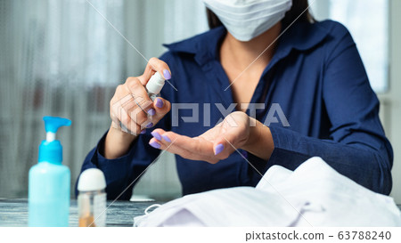 Woman wearing protective mask and using sanitizer at home 63788240