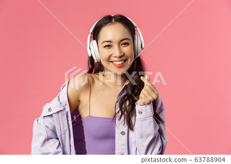 Close-up portrait of attractive happy young modern asian girl, listening music in headphones, show korean heart sign, enjoying favorite music or podcast, bought earphones with discount Close-up portrait of attractive happy young modern asian girl, listening music in headphones, show korean heart sign, enjoying favorite music or podcast, bought earphones with discount 63788904