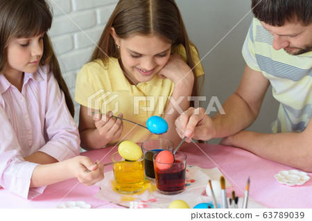 Daddy paint eggs in glasses with colorful dyes. 63789039