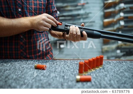Male person with rifle loads ammo in gun shop Male person with rifle loads ammo in gun shop 63789776