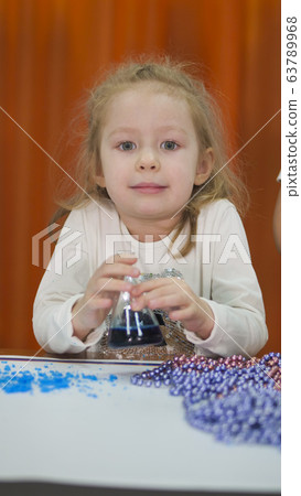 Child is holding flasks of colored liquid. Chemical experiments for children. Fun experiments for children. Children have fun and learn. Bright children's emotions. 63789968