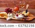 Assortment of cheese with fruits, grapes, nuts, glass with wine and cheese knife on a wooden serving tray. 63792198