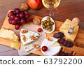 Assortment of cheese with fruits, grapes, nuts, glass with wine and cheese knife on a wooden serving tray. 63792200