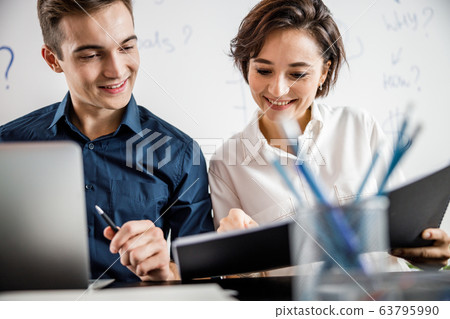 Smiling two employees holding papers in the office Smiling two employees holding papers in the office 63795990