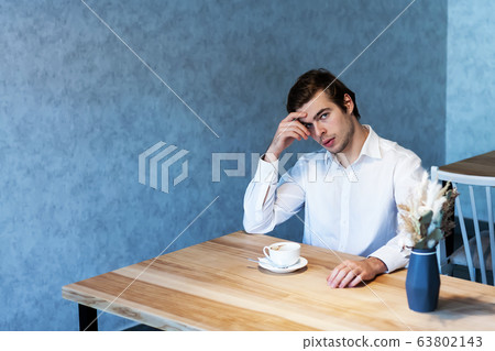 Handsome male looking away sitting at table in cafeteria 63802143